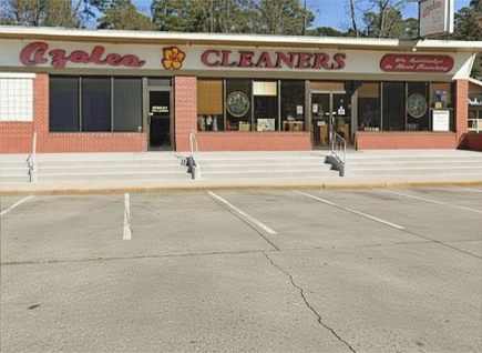 Storefront of Azalea Cleaners with large windows, two entrance doors, brick facade, and empty parking spaces in front.